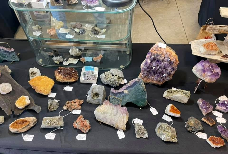 A mixed mineral display featuring crystals, rough specimens and labeled pieces from a show collection.