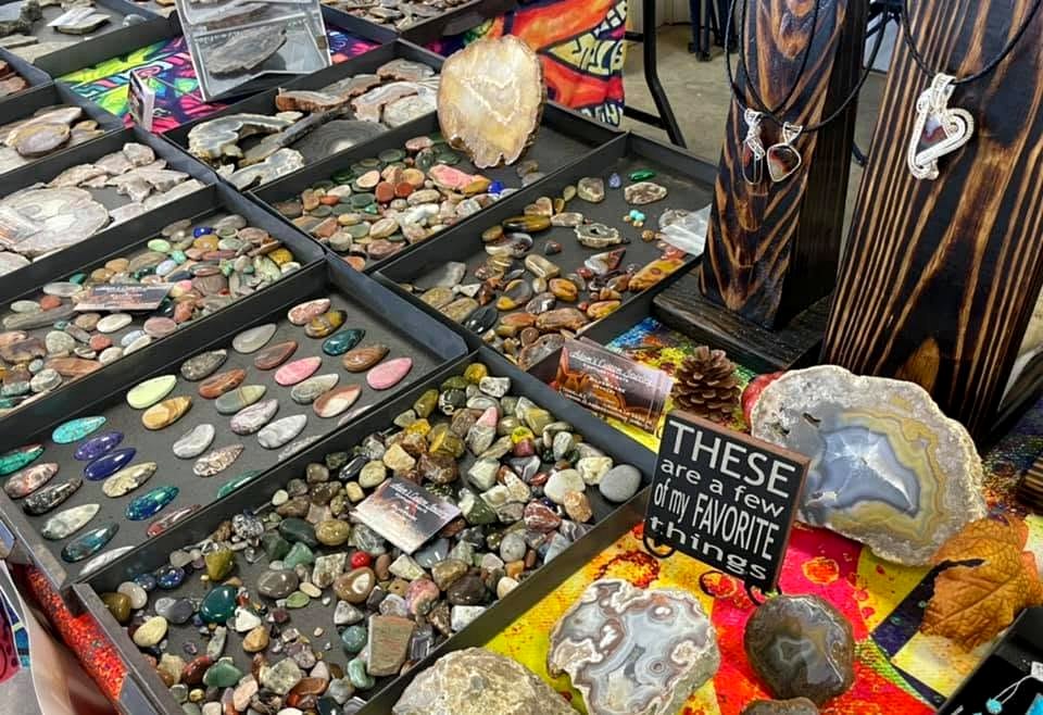 A vendor-style lapidary display with polished stones, cabochons, rough material and finished pieces.