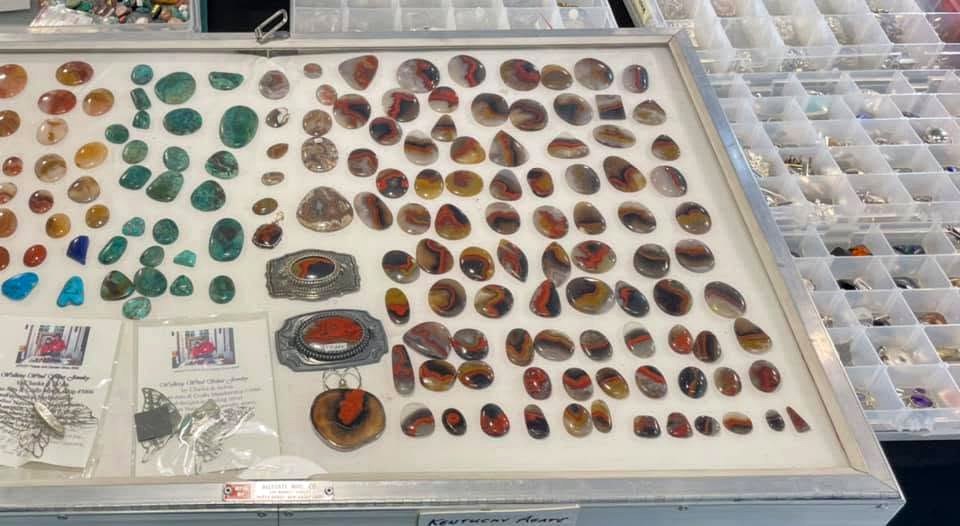 An organized case of polished cabochons and small mineral specimens prepared for display.